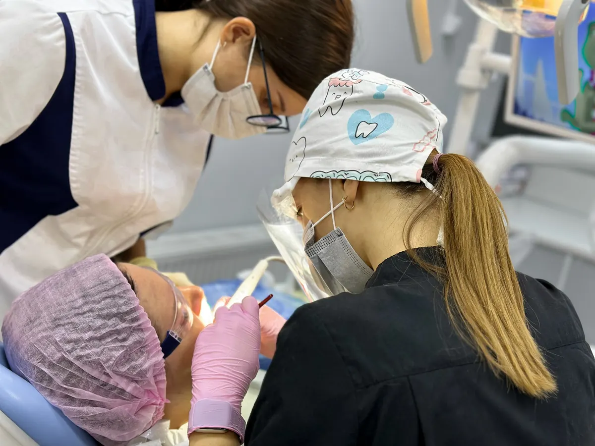 Врач и ассистент работают в четыре руки во время приёма в клинике «Альфа Стоматология»